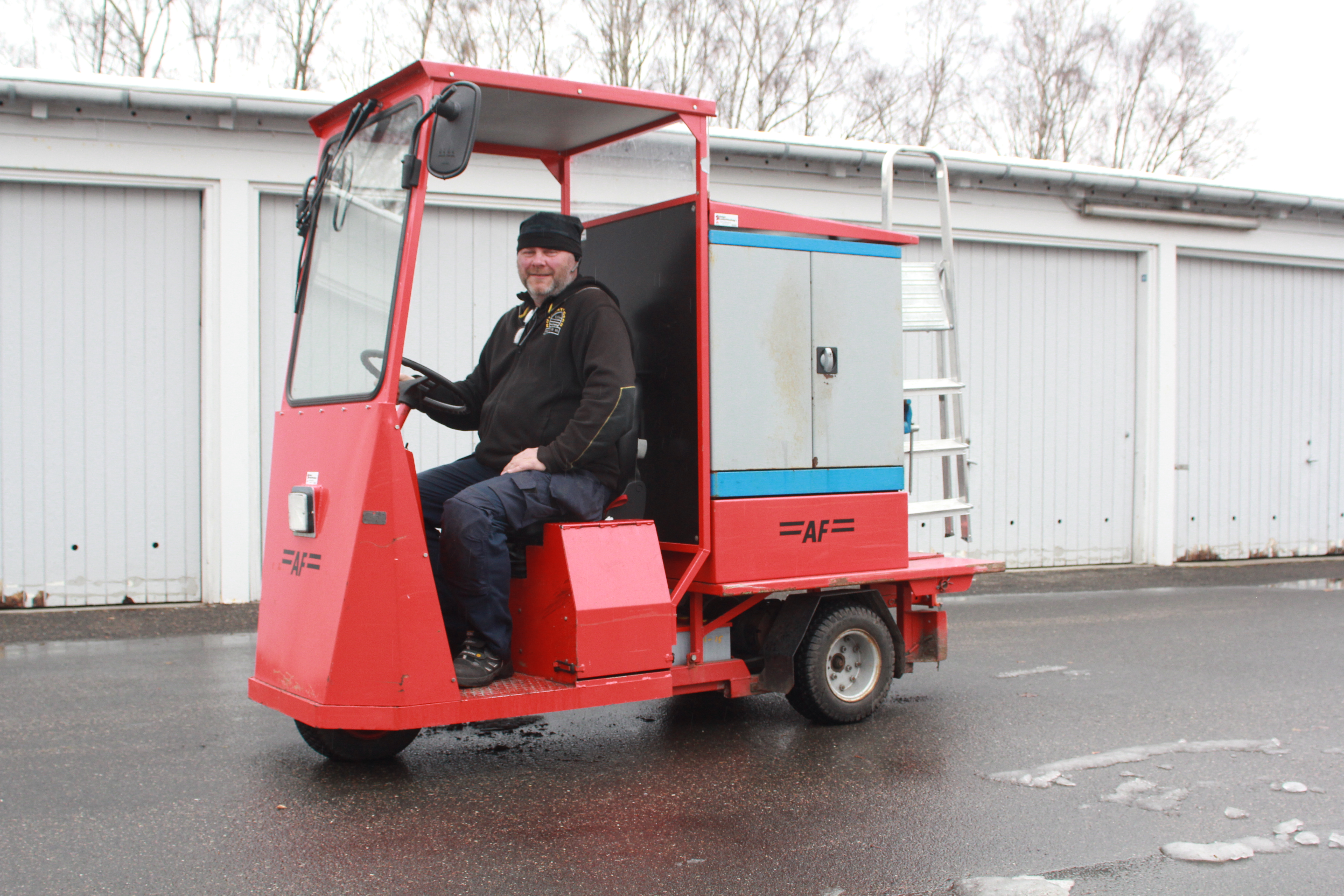 Ejendomsmesterassistent Peter Dan Jensen med sin røde, trehjulede elbil, der gør det let at løse uventede småopgaver hos en beboer.
